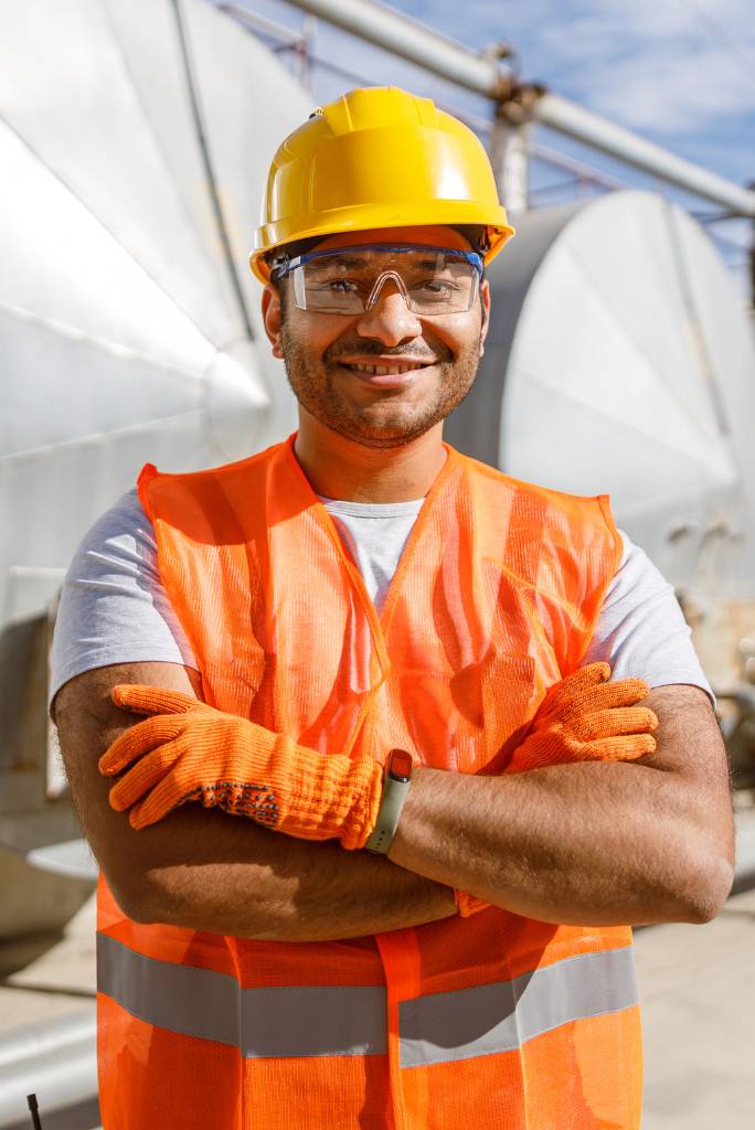 Trabajador industrial sonriente con chaleco reflectante, casco y guantes de seguridad