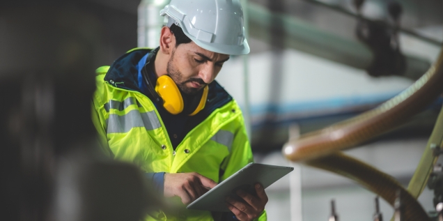 Técnico con casco y chaleco de seguridad revisando un estudio normativo en una tableta