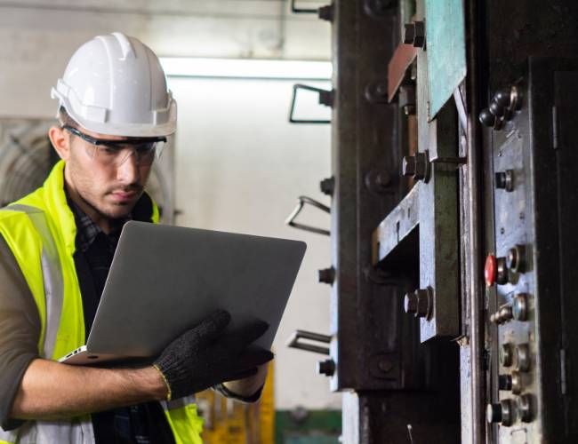 Técnico con casco y laptop frente a un tablero eléctrico industrial